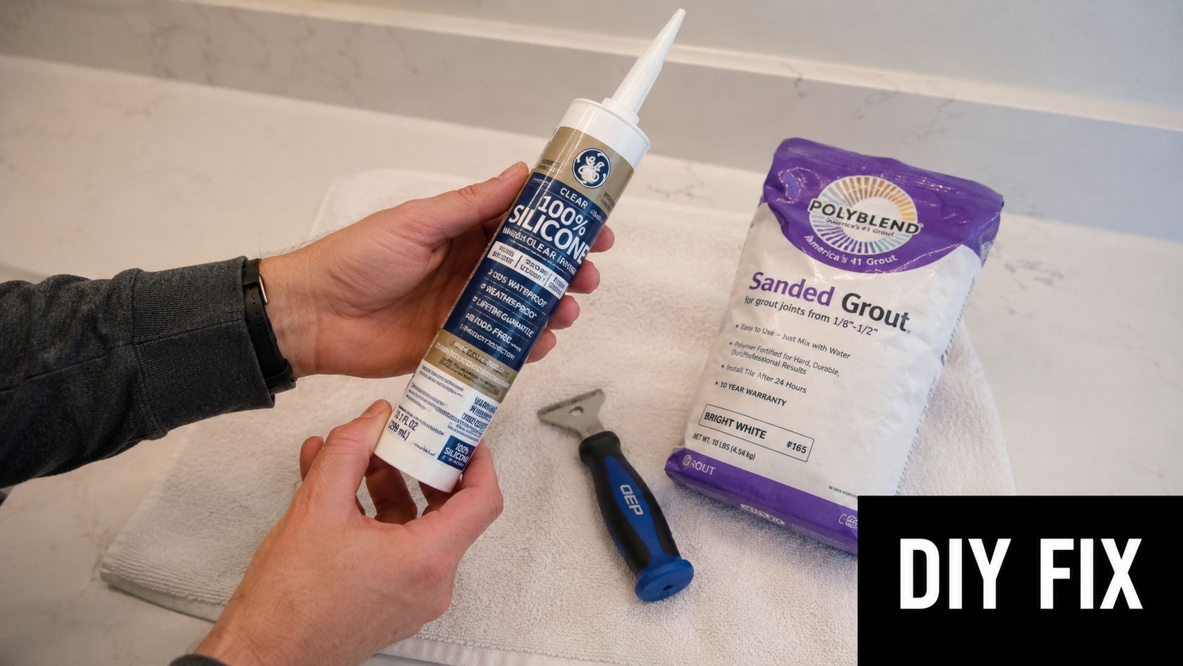 A person holding a tube of silicone caulk alongside a bag of sanded grout and a scraping tool.