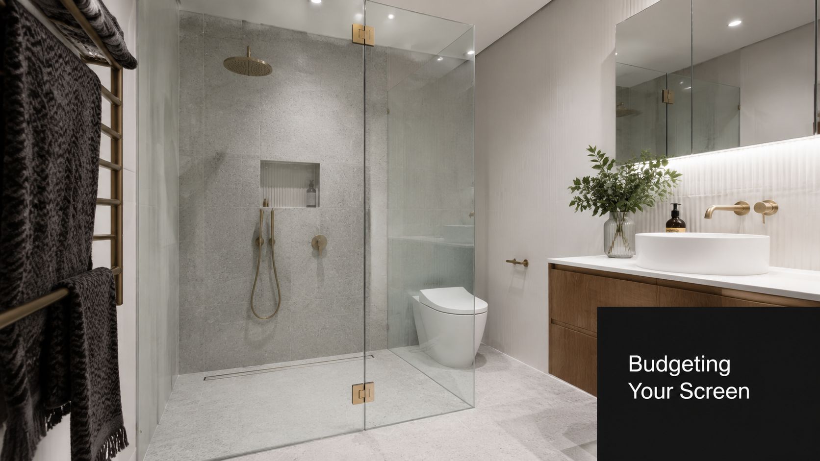 A modern bathroom featuring a frameless glass shower screen with brushed brass fixtures and wood vanity.
