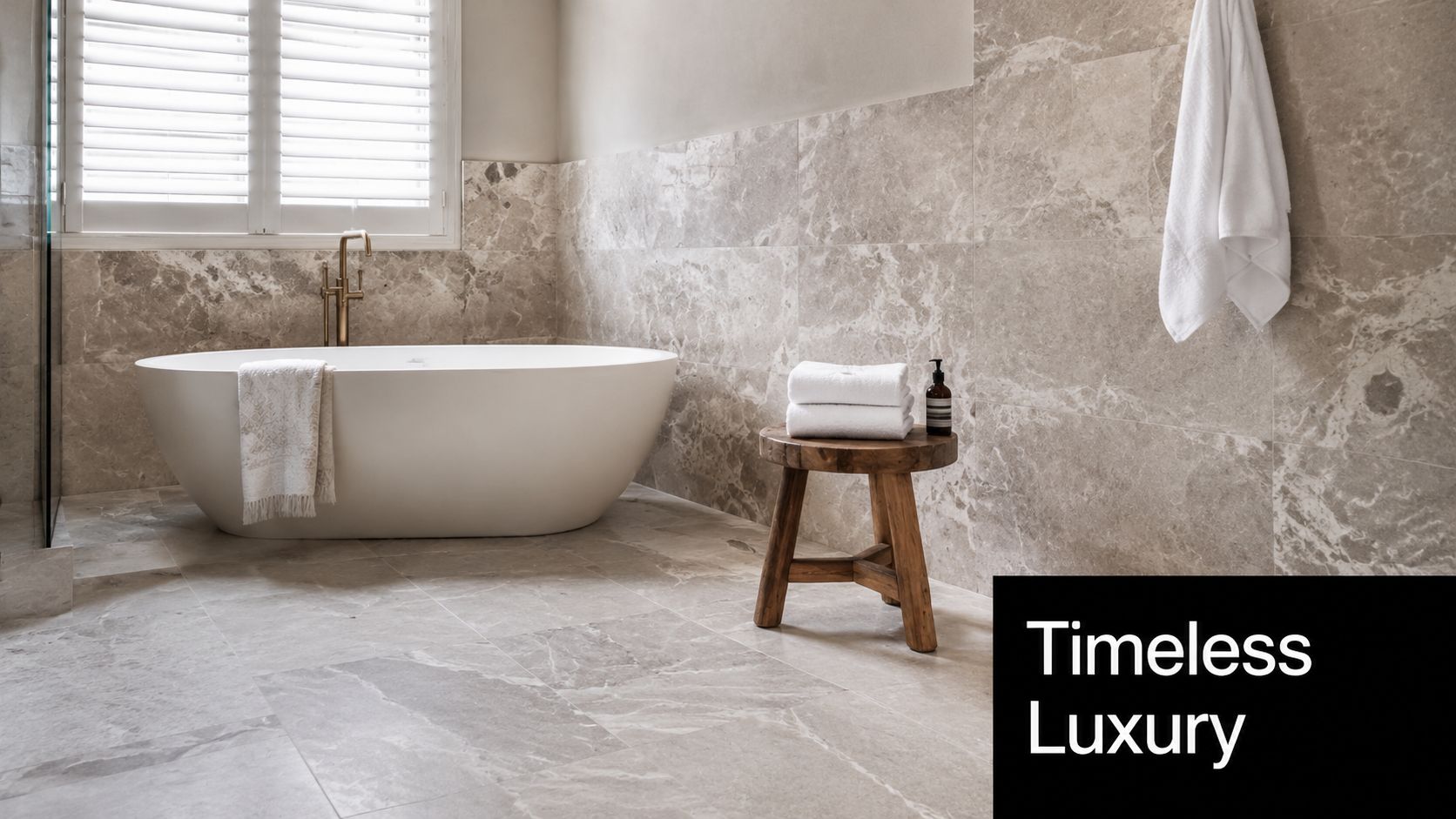 A luxurious bathroom featuring elegant natural stone tiles, a white freestanding bathtub, and a wooden stool.